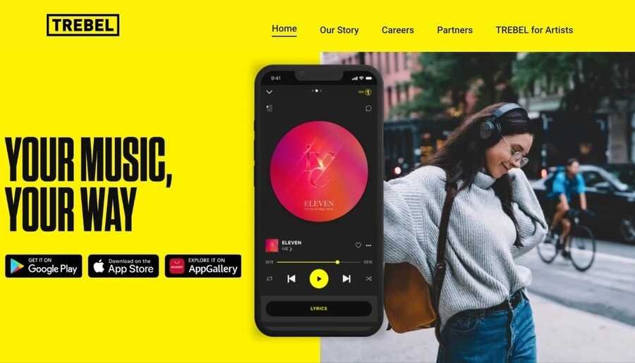 Skærmbillede af Trebels hjemmeside med sloganet 'YOUR MUSIC, YOUR WAY' på en gul baggrund, download-knapper til app-butikker, og en smartphone der viser musikafspilleren foran en kvinde med hovedtelefoner.