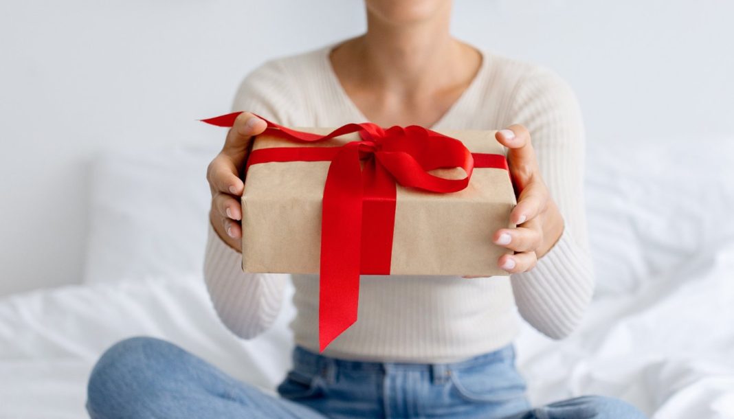 En pige med en gave i hænderne sidder på sengen.