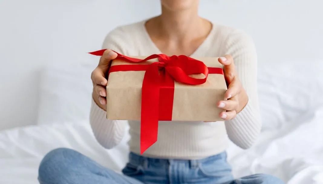giveaway En pige med en gave i hænderne sidder på sengen.