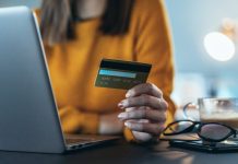 Pigen foran en bærbare computer med et kreditkort i hånden.