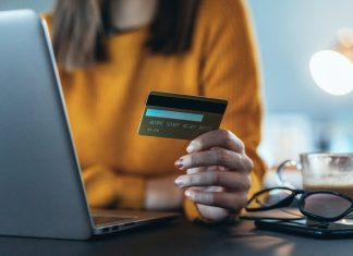 Pigen foran en bærbare computer med et kreditkort i hånden.