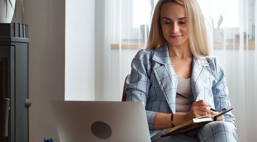 En pige med en notesbog sidder foran en bærbar computer