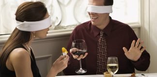 En mand og en kvinde drikker vin ved et bord med bind for øjnene.