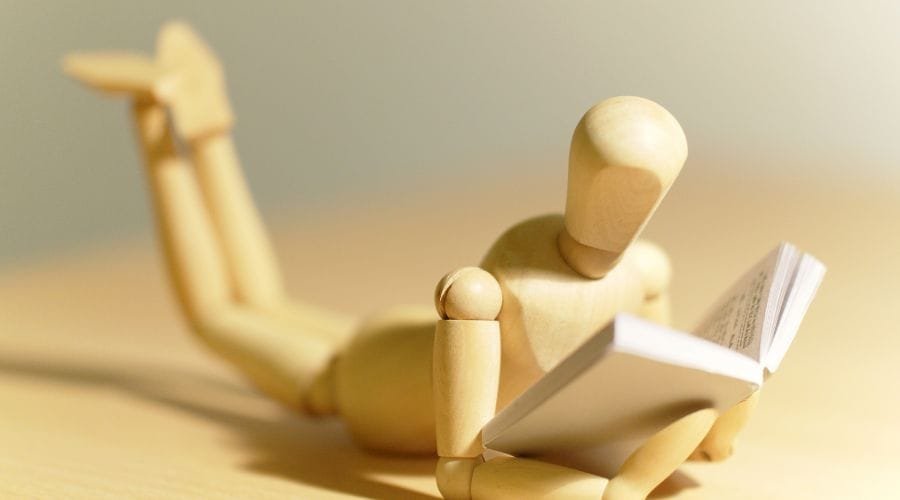 En træmand ligger på gulvet med en bog.