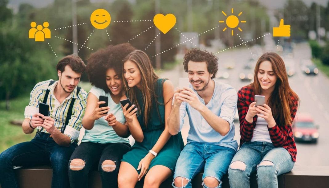 Fem unge mennesker sidder på en bænk med smartphones