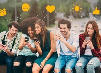 Fem unge mennesker sidder på en bænk med smartphones