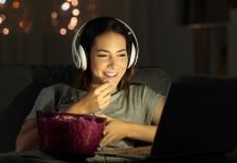 Pige med høretelefoner foran en laptop med popcorn på bordet