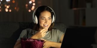 Pige med høretelefoner foran en laptop med popcorn på bordet