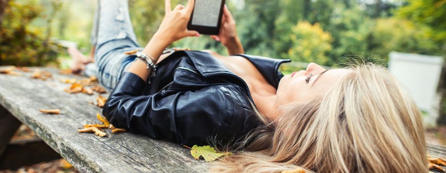 Blond pige ligger på en bænk med en e-bog i hænderne