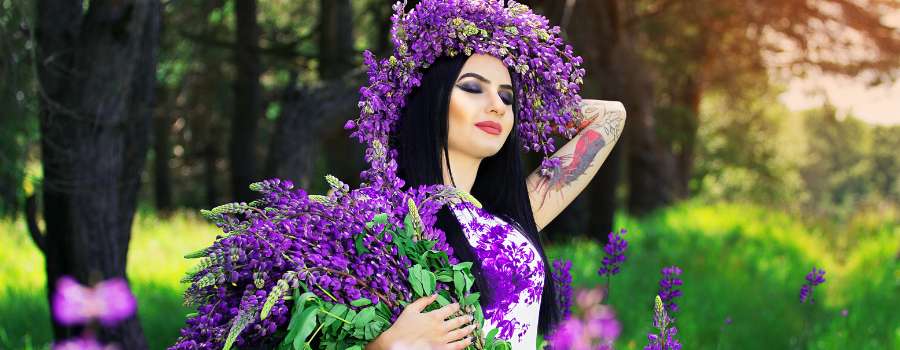Pigemodel i skov med buket af lilla blomster og krans på hovedet lavet af lilla blomster