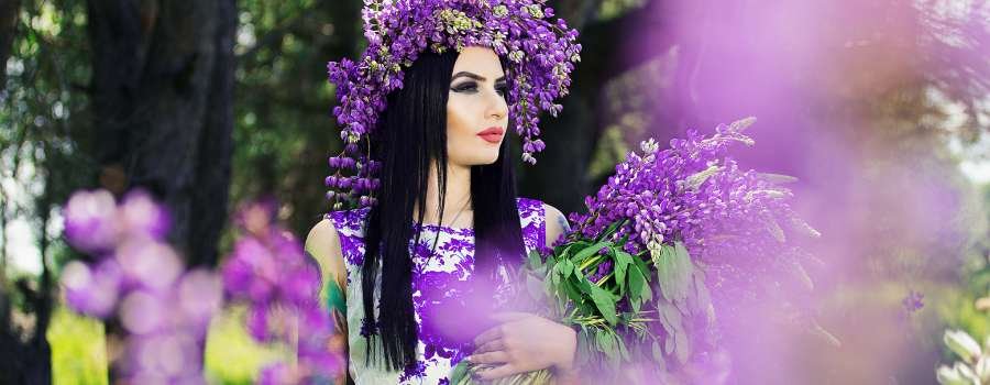 Pigemodel i skov med buket af lilla blomster og krans på hovedet lavet af lilla blomster