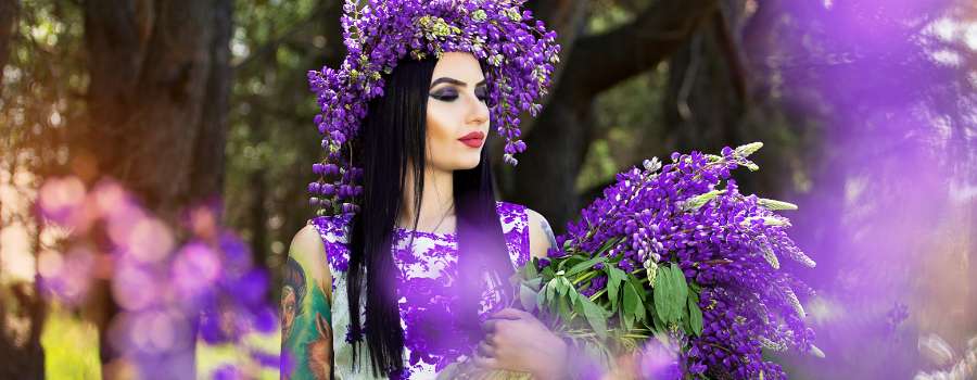 Pigemodel i skov med buket af lilla blomster og krans på hovedet lavet af lilla blomster