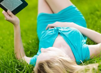 En lyshåret pige med en e-bog i hænderne ligger på græsset