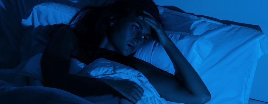 En pige ligger i sengen med åbne øjne i halvmørket.