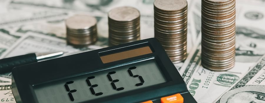 En lommeregner med fees skrevet på skærmen ligger på dollarsedler ved siden af stakke af mønter