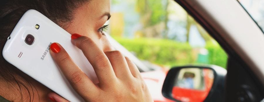 Pigen bag rattet taler i sin telefon, en hvid Samsung