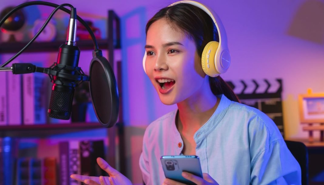 En pige iført høretelefoner og med en telefon i hånden foran en mikrofon med åben mund