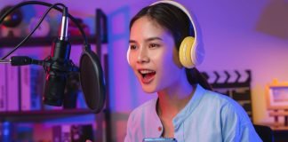 En pige iført høretelefoner og med en telefon i hånden foran en mikrofon med åben mund