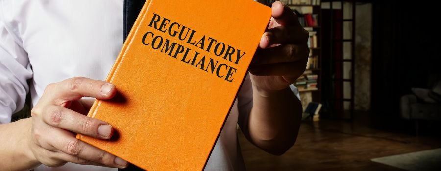 En mand holder en orange bog op med påskriften: Regulatory Compliance