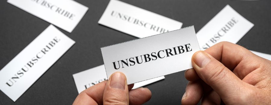 Et stykke papir med påskriften "unsubscribe" i menneskehænder over et bord med lignende papirer spredt ud over det