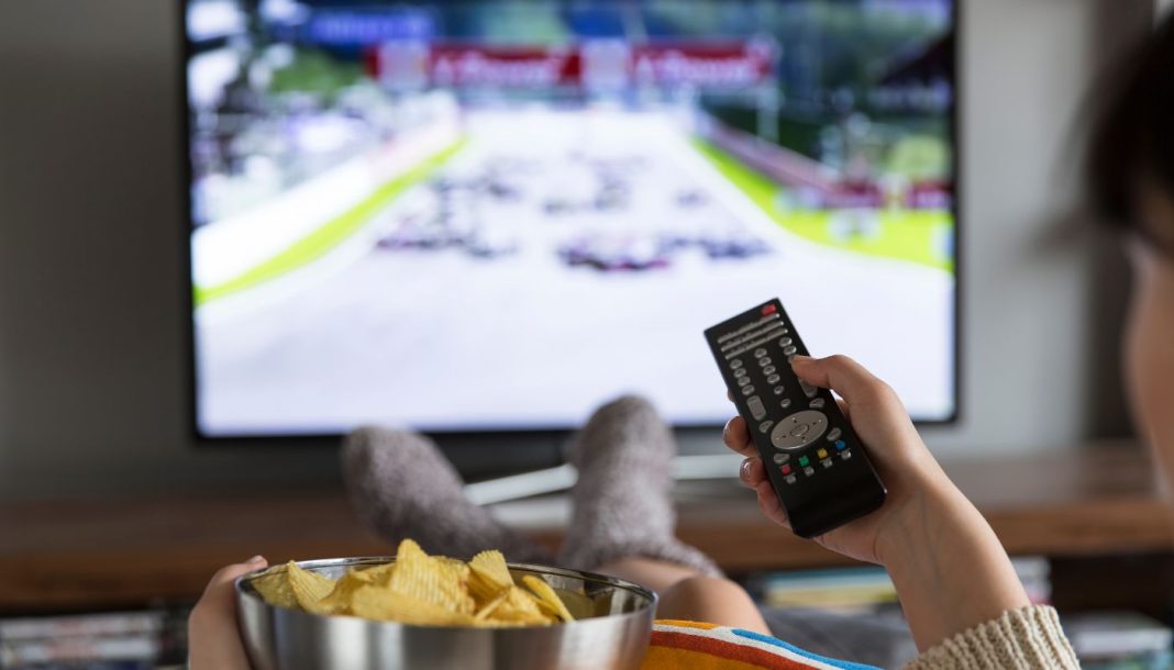 En pige med en skål popcorn og en fjernbetjening i hånden sidder foran fjernsynet