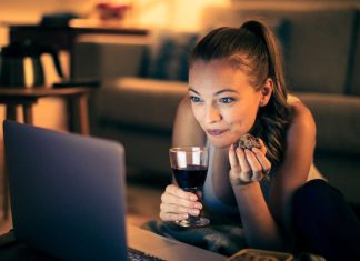 En pige med et glas vin sidder i en sofa foran en bærbar computer