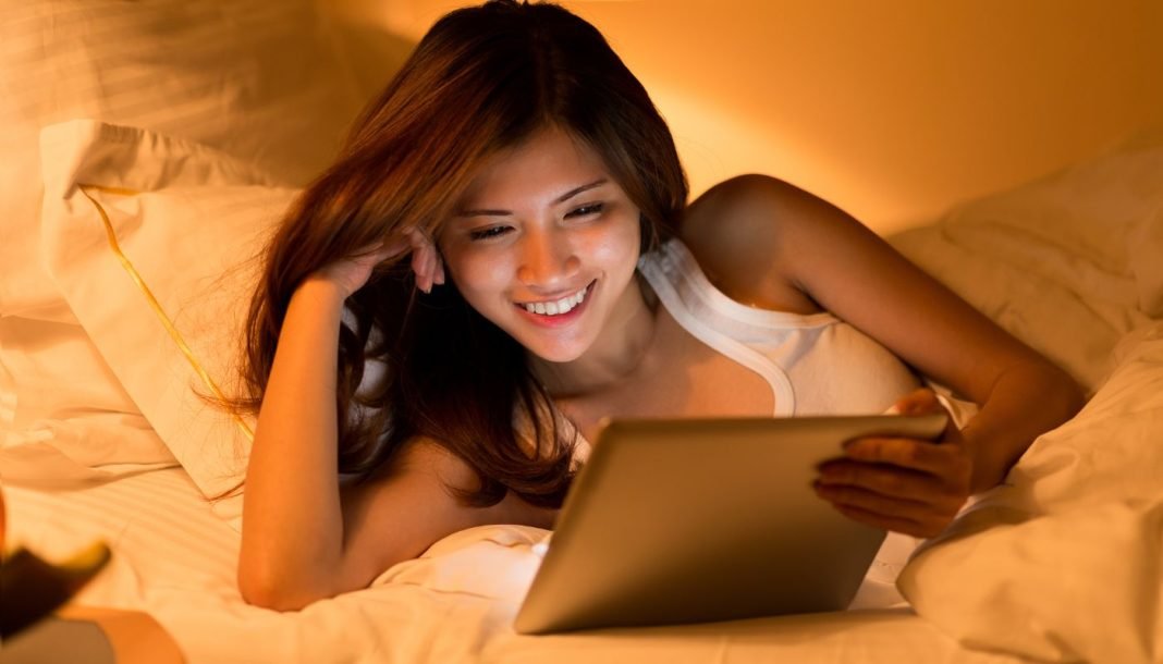 girl-watching-tablet Asiatisk pige med en tablet i hænderne ligger i sengen