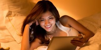 Asiatisk pige med en tablet i hænderne ligger i sengen