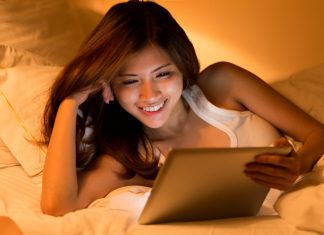 Asiatisk pige med en tablet i hænderne ligger i sengen