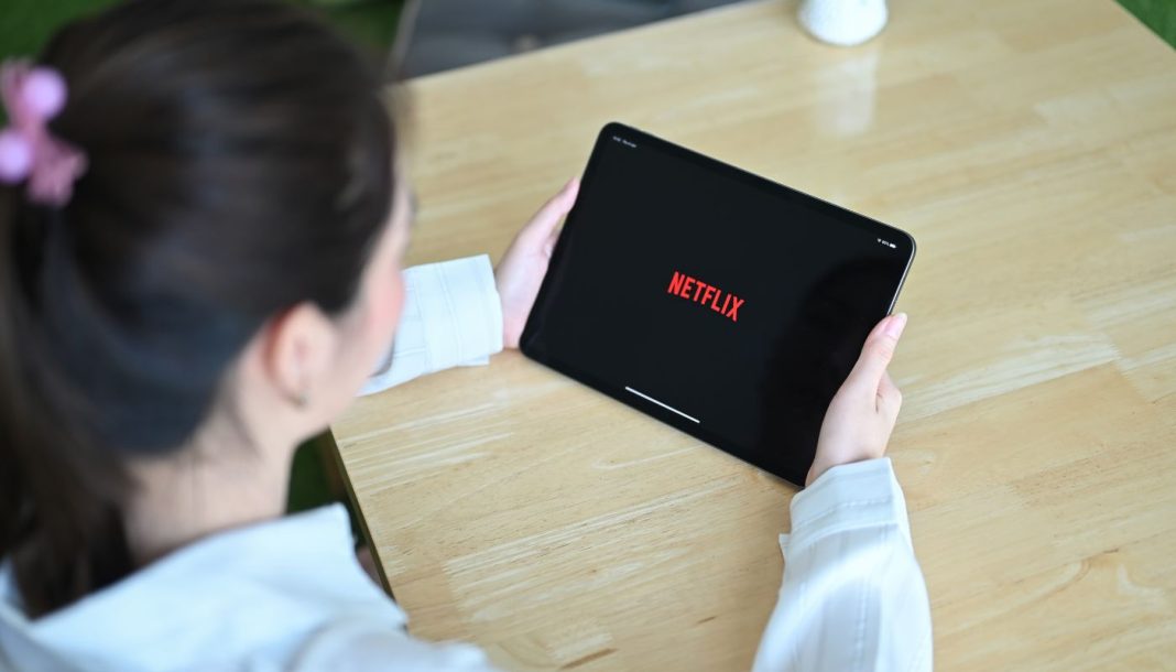 En pige med en tablet i hænderne sidder ved et skrivebord, Netflix-logo på tabletskærmen