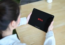 En pige med en tablet i hænderne sidder ved et skrivebord, Netflix-logo på tabletskærmen