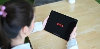 En pige med en tablet i hænderne sidder ved et skrivebord, Netflix-logo på tabletskærmen