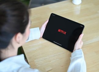 En pige med en tablet i hænderne sidder ved et skrivebord, Netflix-logo på tabletskærmen