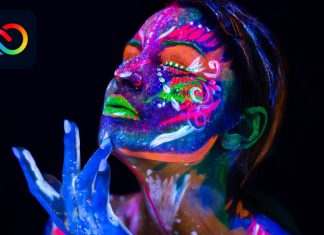 Kvinde med neonlys malet på ansigtet og hænderne på en sort baggrund, med Adobe Creative Cloud logo i øverste venstre hjørne.