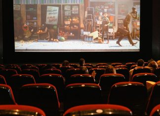 Usikker på, hvad du skal se på dine streamingtjenester? Tryk på denne knap Biografsal med mennesker, der ser en animationsfilm på en stor skærm, med delvist fyldte røde sæder.