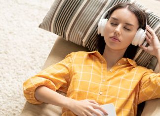 Pige med hovedtelefoner ligger på en sofa og lytter til musik med lukkede øjne.