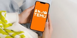 En persons hænder, der holder en smartphone med TEMU-logoet på en orange baggrund.