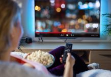 Kvinde ser TV med fjernbetjening og popcorn i hånden.