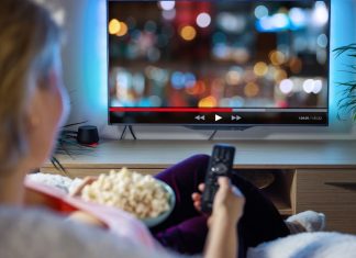 Kvinde ser TV med fjernbetjening og popcorn i hånden.