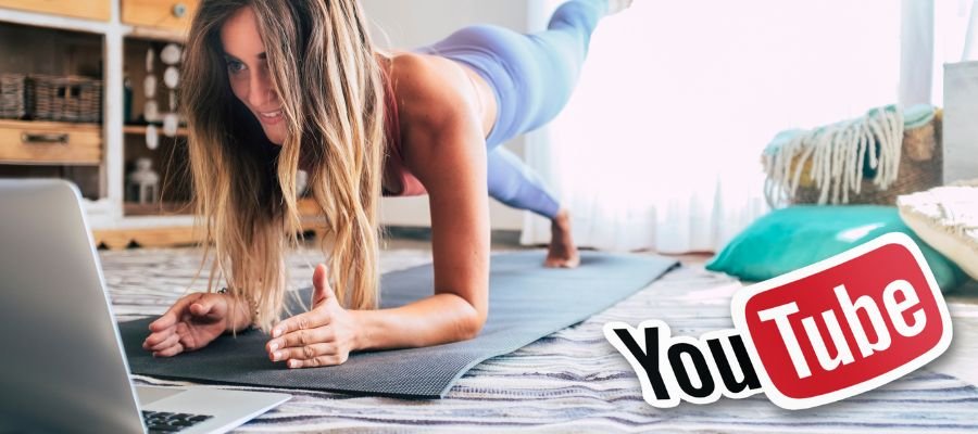En pige i planken på en yogamåtte, der kigger på en bærbar computer, deltager i en online fitness- eller yogalektion.