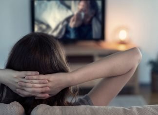 De 10 bedste streamingtjenester til dokumentarfilm En kvinde sidder på en sofa med hænderne bag hovedet og ser fjernsyn.