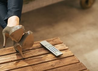 6 niche-streamingtjenester, der tilbyder mere fokuseret indhold end Netflix Kvinde ben i højhælede sko, afslappet hvilende på et træbord ved siden af en fjernbetjening.