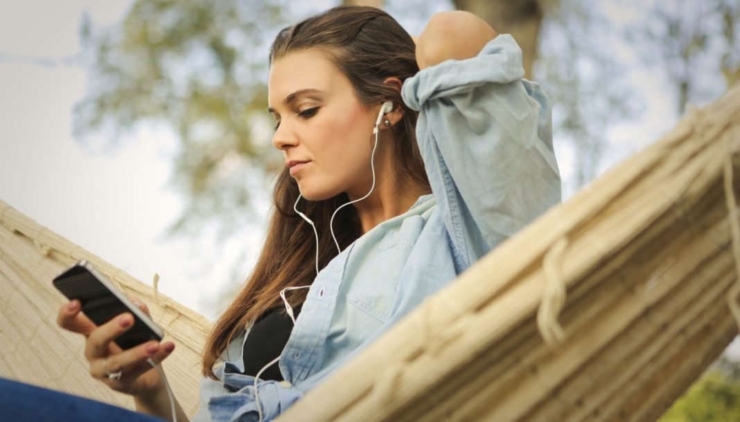 En pige sidder i en hængekøje og lytter til musik med øretelefoner.