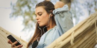 En pige sidder i en hængekøje og lytter til musik med øretelefoner.