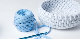 En hæklenål, et nøgle lyseblåt garn og en hæklet hvid kurv.