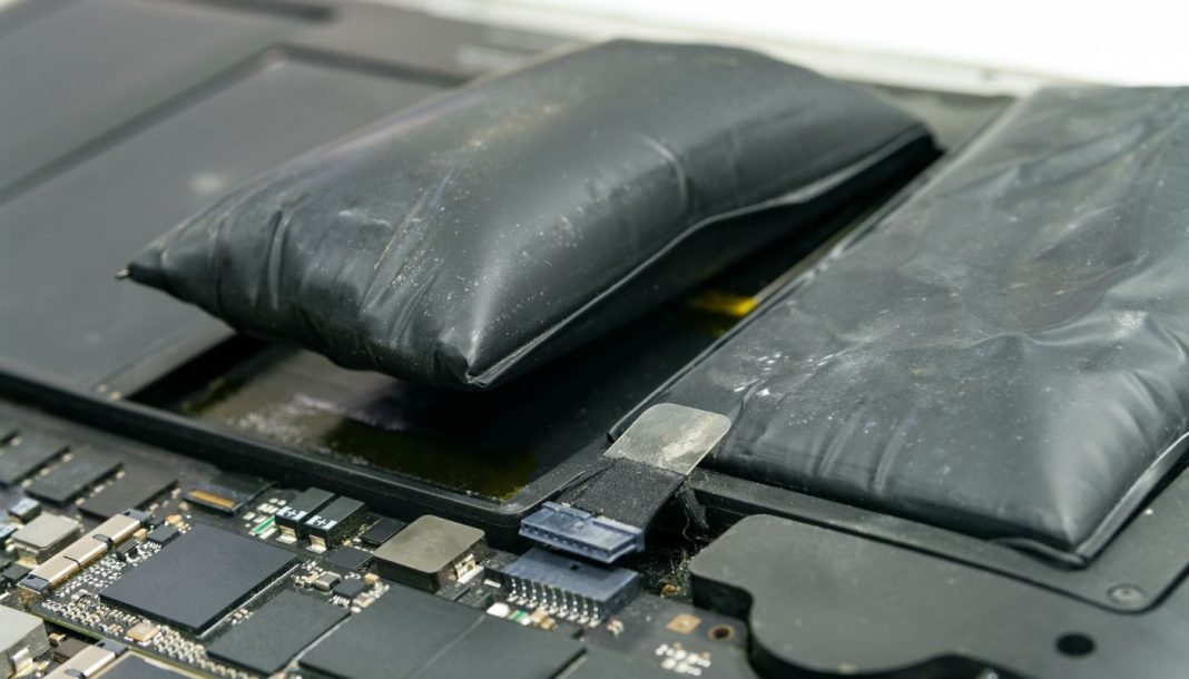 To oppustede, sorte batterier ligger på en grå, slidt overflade. Batterierne er tydeligt hævede og ser deformerede ud, hvilket indikerer en mulig fejlfunktion eller overopladning.