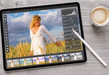 En tablet på et træbord ved siden af en kop kaffe. På tablettens skærm er et foto redigeringsprogram åbent, hvor et billede af en kvinde i en hvid kjole i en mark med høje græsstrå redigeres.