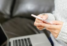 Person bruger en smartphone foran en bærbar computer i sofaen.