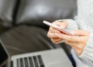 Person bruger en smartphone foran en bærbar computer i sofaen.