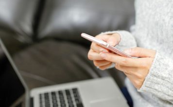 Person bruger en smartphone foran en bærbar computer i sofaen.